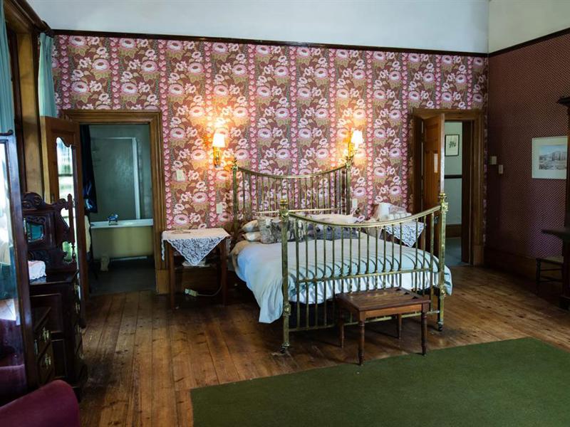 The Family Suite's main room: a brass bed against patterned wallpaper, with the bathroom through one door and the second bedroom through the other