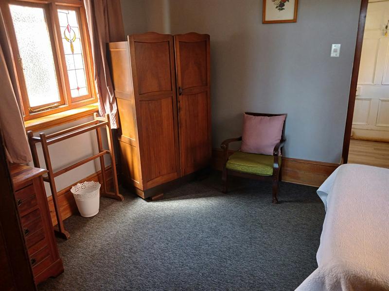 An antique wooden wardrobe and armchair beside a stained glass window in the Garden Room
