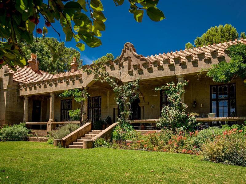 The homestead seen across the lawn, framed by the leaves of a garden tree