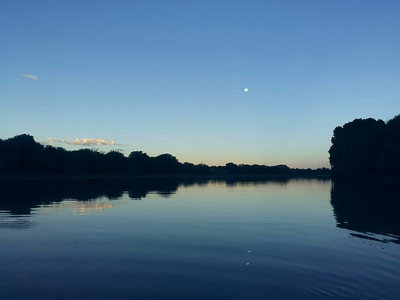 The moon rising over the river at dusk, reflected in still blue water