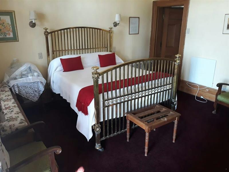 The Red Room: a brass poster double bed in white linen with deep red cushions, wall sconces either side and a deep red carpet