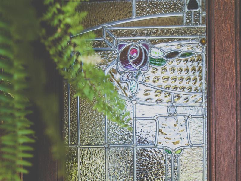Detail of the leaded and stained glass front door, with a fern in the foreground