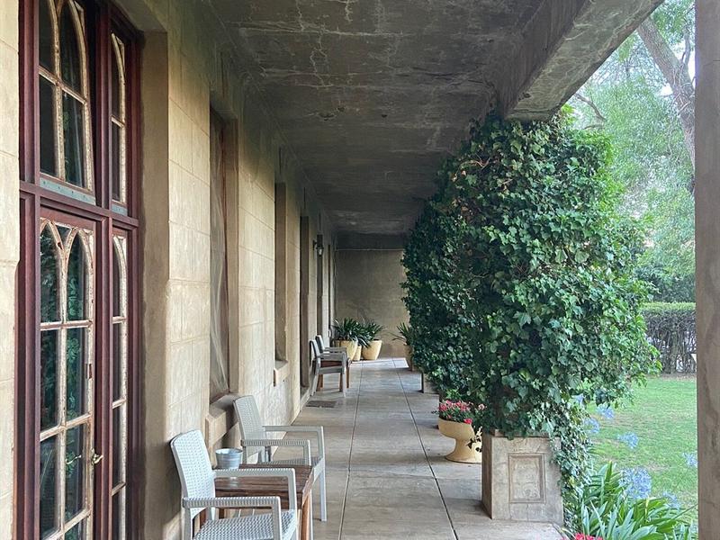 The verandah running the length of the house, with chairs and potted plants between the stone columns